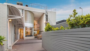 Un edificio moderno con facciata in vetro curvo, una terrazza sul tetto con posti a sedere e un vialetto lastricato.