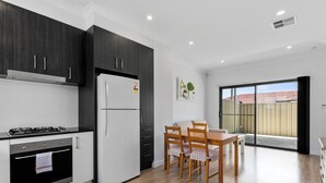 Eine moderne Küche mit dunklen Schränken, einem weißen Kühlschrank, einem Herd und einem Essbereich mit Tisch und Stühlen.