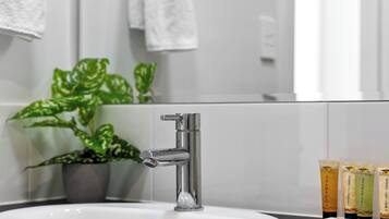 Et badeværelse med en moderne vask, en potteplante og en række toiletartikler.