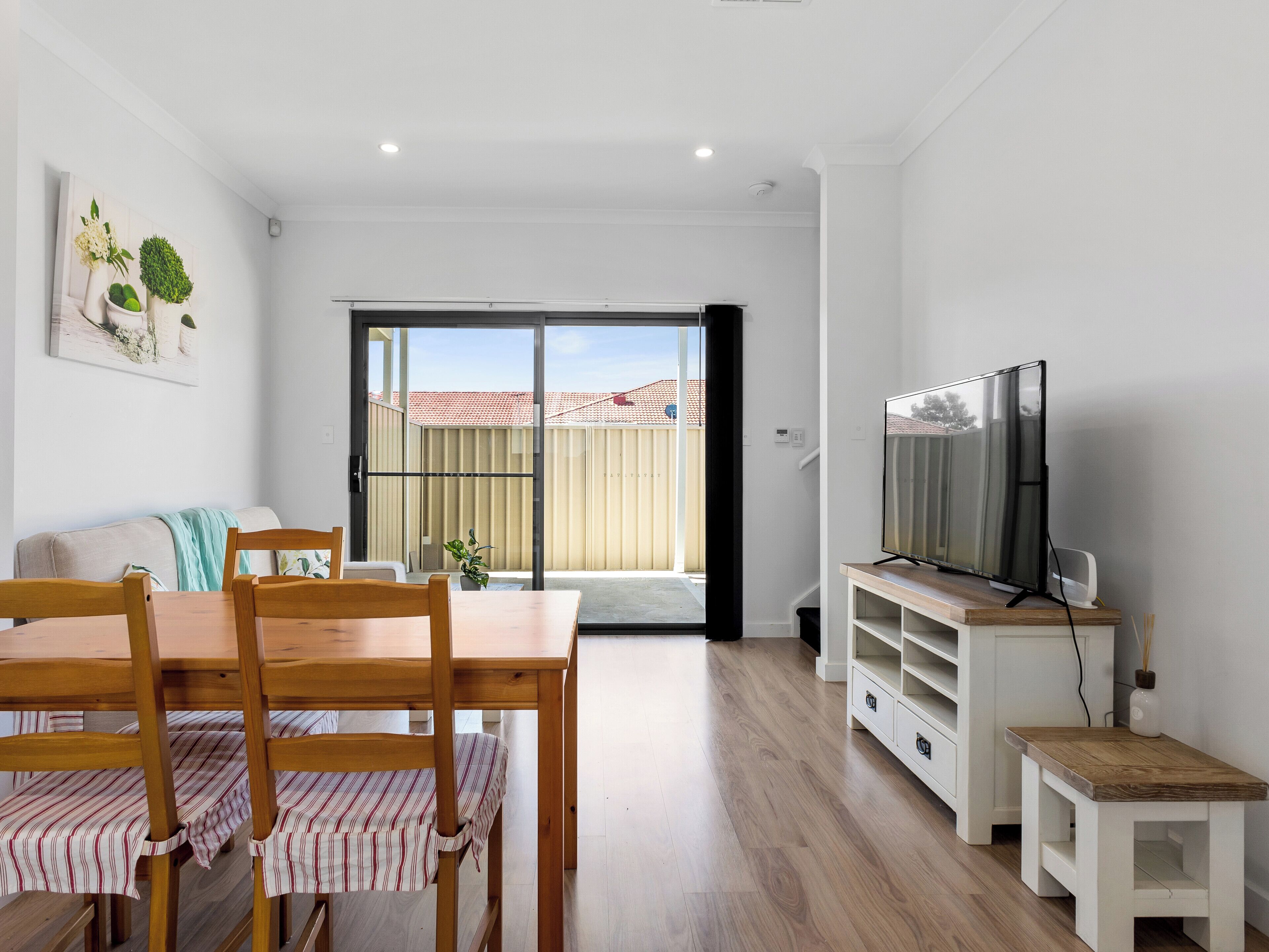 Un salon moderne comprenant une table à manger, des chaises, un téléviseur et une porte-fenêtre coulissante donnant sur un balcon.