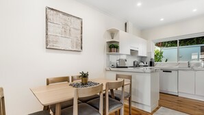 A modern kitchen with white cabinets, a dining table with chairs, and a large decorative wall piece.