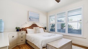 A bedroom with a bed, bedside tables, a nightstand, a ceiling fan, and a window with blinds.