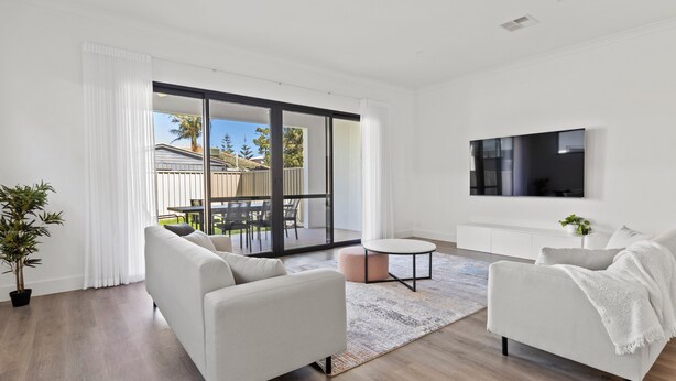A modern living room with a sofa, a coffee table, and a TV mounted on the wall. - Swainson on Lexington (Henley Beach South)