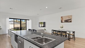 A modern kitchen with a large island, stainless steel appliances, and a dining area with a table and chairs. - Swainson on Lexington (Henley Beach South)