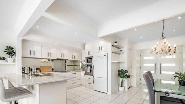 Uma cozinha moderna com armários brancos, uma ilha central e uma área de jantar com mesa e cadeiras de vidro.
