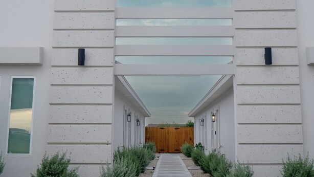 A modern building with a central wooden door, flanked by white walls and small green bushes. - Modern 2-bed, 2-bath home with WiFi, Smart TVs, coffee, tea, and cereal included (Weslaco)
