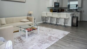 A modern living room with a sofa, a glass coffee table, and a bar area with stools. - Modern 2-bed, 2-bath home with WiFi, Smart TVs, coffee, tea, and cereal included (Weslaco)