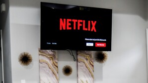 A modern living room with a mounted TV displaying the Netflix logo, a white entertainment unit below, and two decorative wall art pieces. - Modern 2-bed, 2-bath home with WiFi, Smart TVs, coffee, tea, and cereal included (Weslaco)