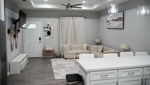 A modern living room with a sofa, a dining area with a white table, and a ceiling fan. - Modern 2-bed, 2-bath home with WiFi, Smart TVs, coffee, tea, and cereal included (Weslaco)