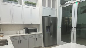 A modern kitchen with white cabinets, a stainless steel refrigerator, and a microwave. - King Condo In Panama City Beach Resort Amenities Hot Tub Downtown Pier Park (Panama City)