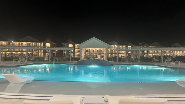 A nighttime view of a hotel pool area with a clear pool, lounge chairs, and a covered seating area. - King Condo In Panama City Beach Resort Amenities Hot Tub Downtown Pier Park (Panama City)