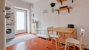 A kitchen with a washing machine, a dining table with chairs, and wall-mounted shelves.