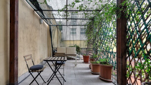 A covered patio with a table and chairs, potted plants, and a wooden trellis.