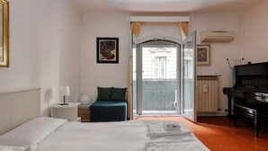 A hotel room with a bed, a piano, a balcony with a view, and a door leading outside.