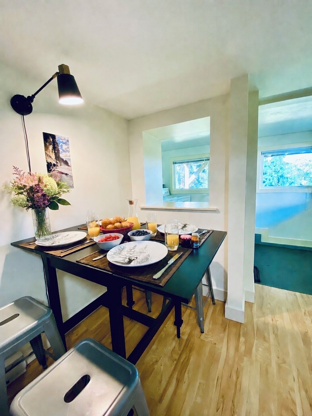 A dining area with a table set for breakfast, a vase with flowers, and a picture on the wall.