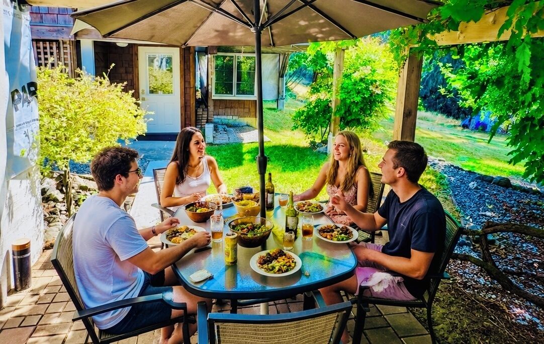 Eine Gruppe von Menschen speist an einem Tisch im Freien mit Blick auf einen Garten.