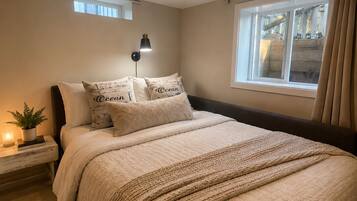 Un dormitorio con cama, mesita de noche, lámpara, ventana y cortinas.