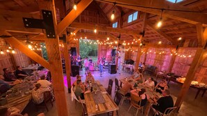 An indoor venue with wooden beams and string lights, featuring tables and chairs for dining and socializing. - The Range Vintage Trailer Resort (Ennis)