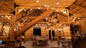 A wooden interior with exposed beams, string lights, and a central dining area with tables and chairs. - The Range Vintage Trailer Resort (Ennis)