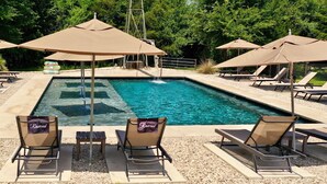 A swimming pool with lounge chairs and umbrellas, surrounded by trees. - The Range Vintage Trailer Resort (Ennis)