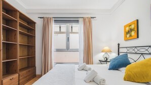 A bedroom with a bed, a wooden wardrobe, a window with curtains, a bedside table with a lamp, and a painting on the wall. - Home2Book Bright Retreat with Pool, Sardina Beach (Gáldar)