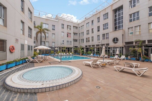 A hotel courtyard with a swimming pool, sun loungers, and a hot tub.