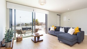 A modern living room with a grey sectional sofa, a wooden coffee table, and a potted plant. - Home2Book Orballo Sea Views Apt, Terrace&Pool (Abades)