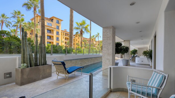 A balcony with a pool, palm trees, and a building in the background.