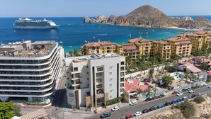 A coastal hotel with multiple floors, a swimming pool, and a view of the sea and boats.