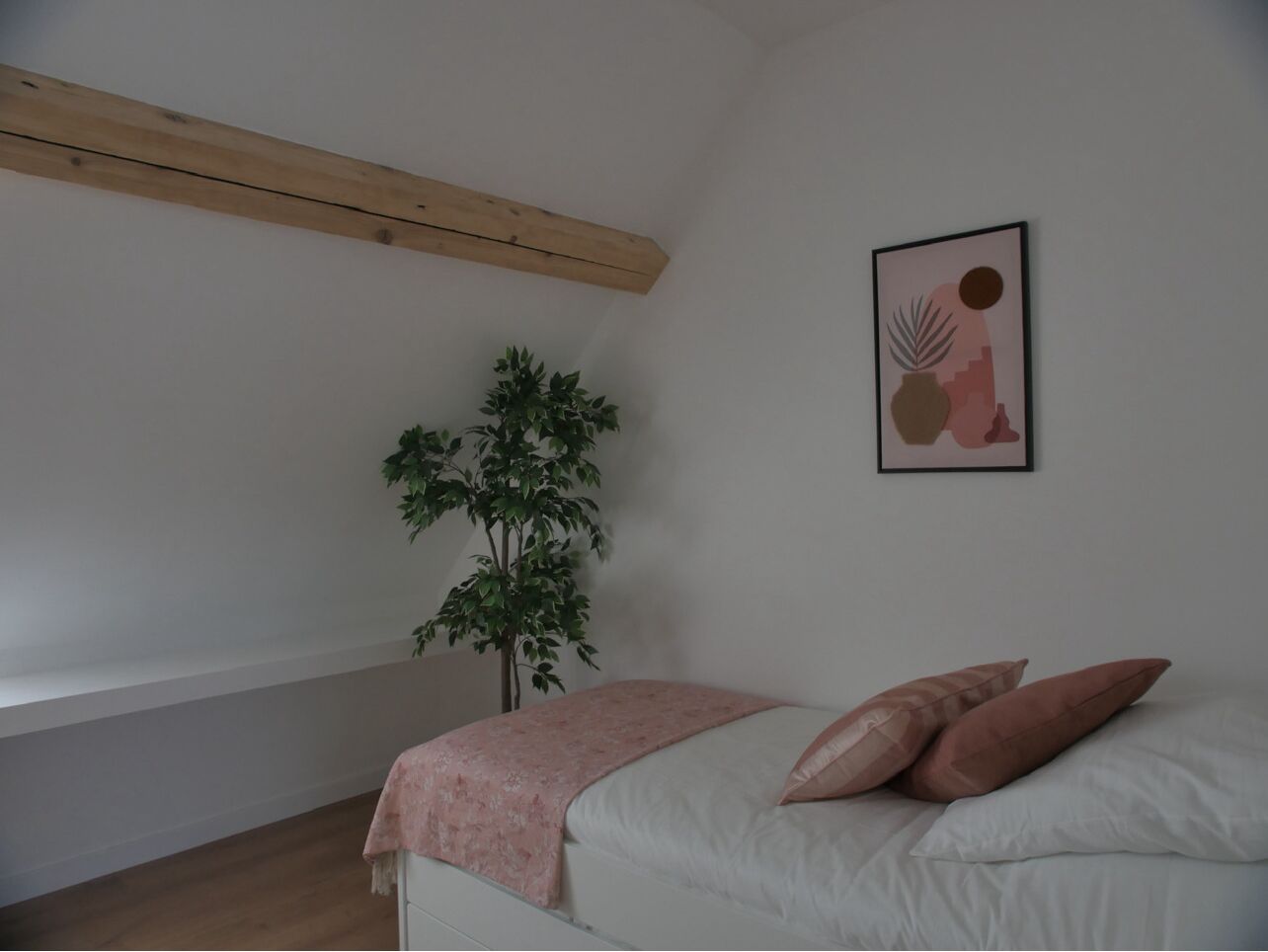 A bedroom with a bed, a plant, and a framed picture on the wall.