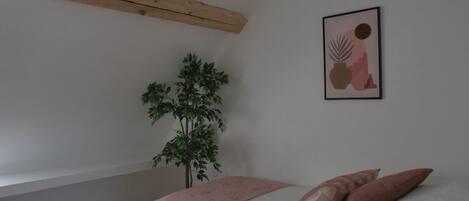 A bedroom with a bed, a plant, and a framed picture on the wall.