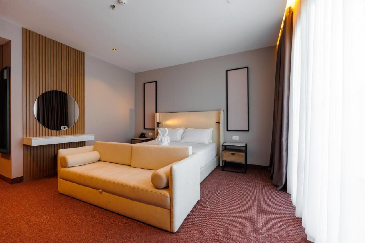 Een hotelkamer met een bed, een slaapbank, een nachtkastje, een spiegel en een aan de muur bevestigde televisie.