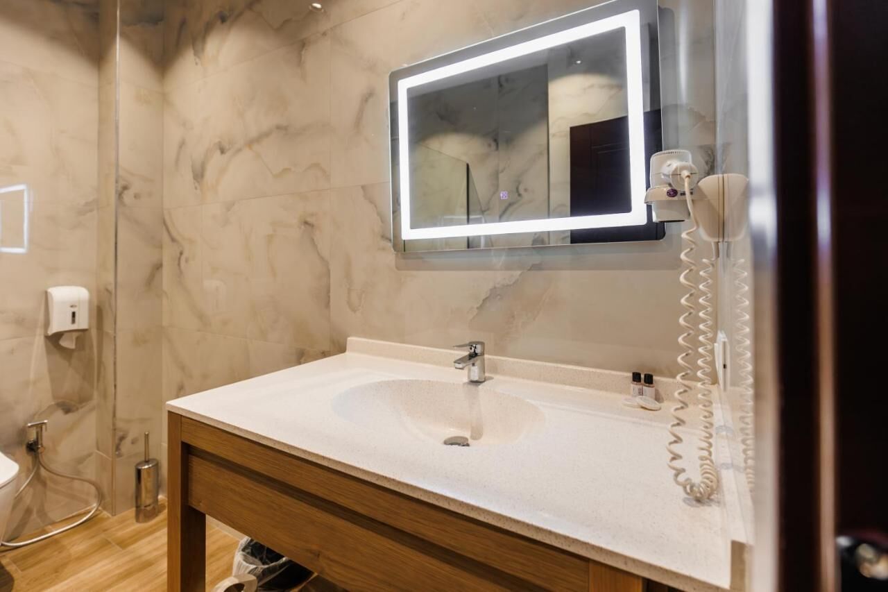 A bathroom with a marble wall, a sink with a mirror above it, and a telephone on the wall.