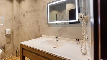 Une salle de bain avec un mur en marbre, un lavabo surmonté d’un miroir et un téléphone fixé au mur.