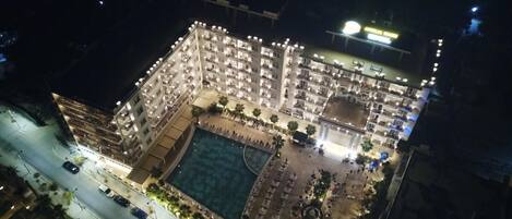 An aerial view of a well-lit hotel with multiple floors, a central courtyard with a pool, and surrounding balconies.