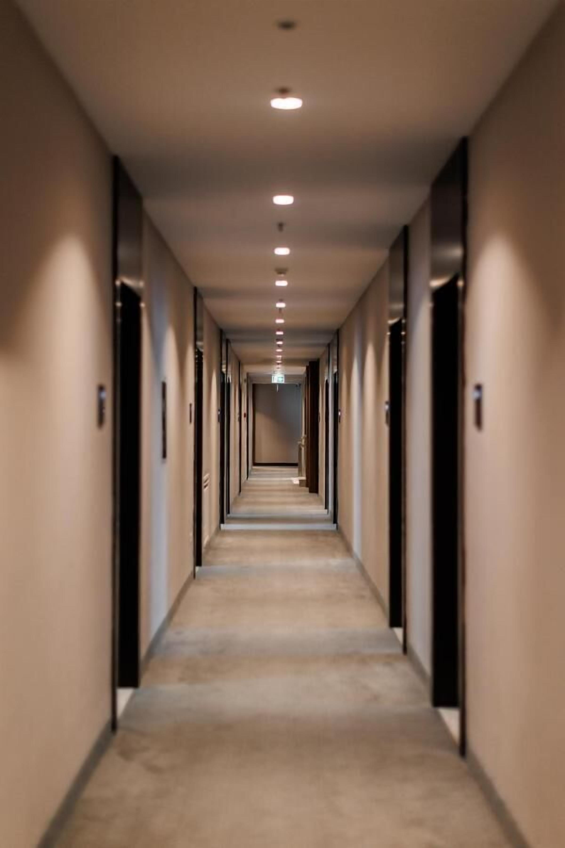 A long, narrow hotel corridor with doors on both sides and a carpeted floor.