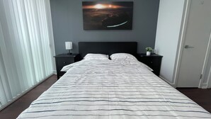 Une chambre à coucher avec un lit, deux tables de chevet, une lampe fixée au mur et une fenêtre avec des stores.
