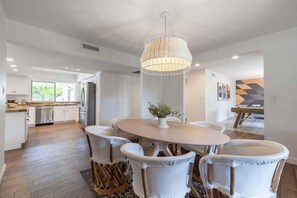 A modern kitchen with white cabinets, a dining area with a round table and white chairs, and a hanging light fixture.