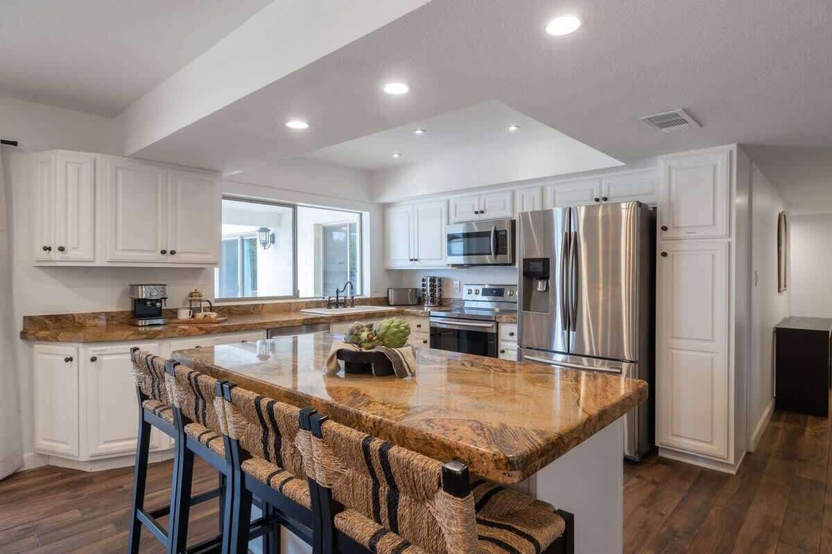 A modern kitchen with white cabinetry, stainless steel appliances, and a granite countertop island with bar stools.