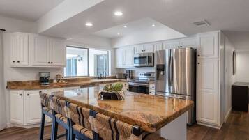 A modern kitchen with white cabinetry, stainless steel appliances, and a granite countertop island with bar stools.
