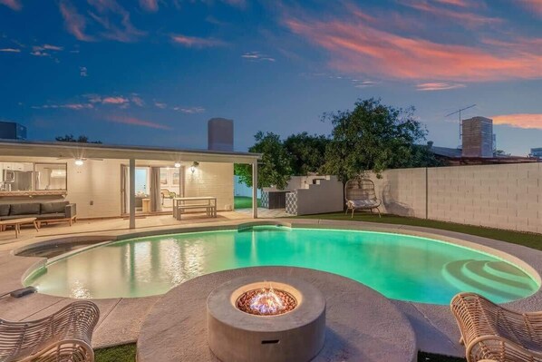 A modern outdoor pool area with a fire pit, lounge chairs, and a well-lit patio.