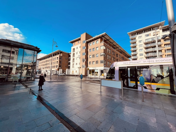 A modern urban square with a tram, buildings with balconies, and a clear sky.