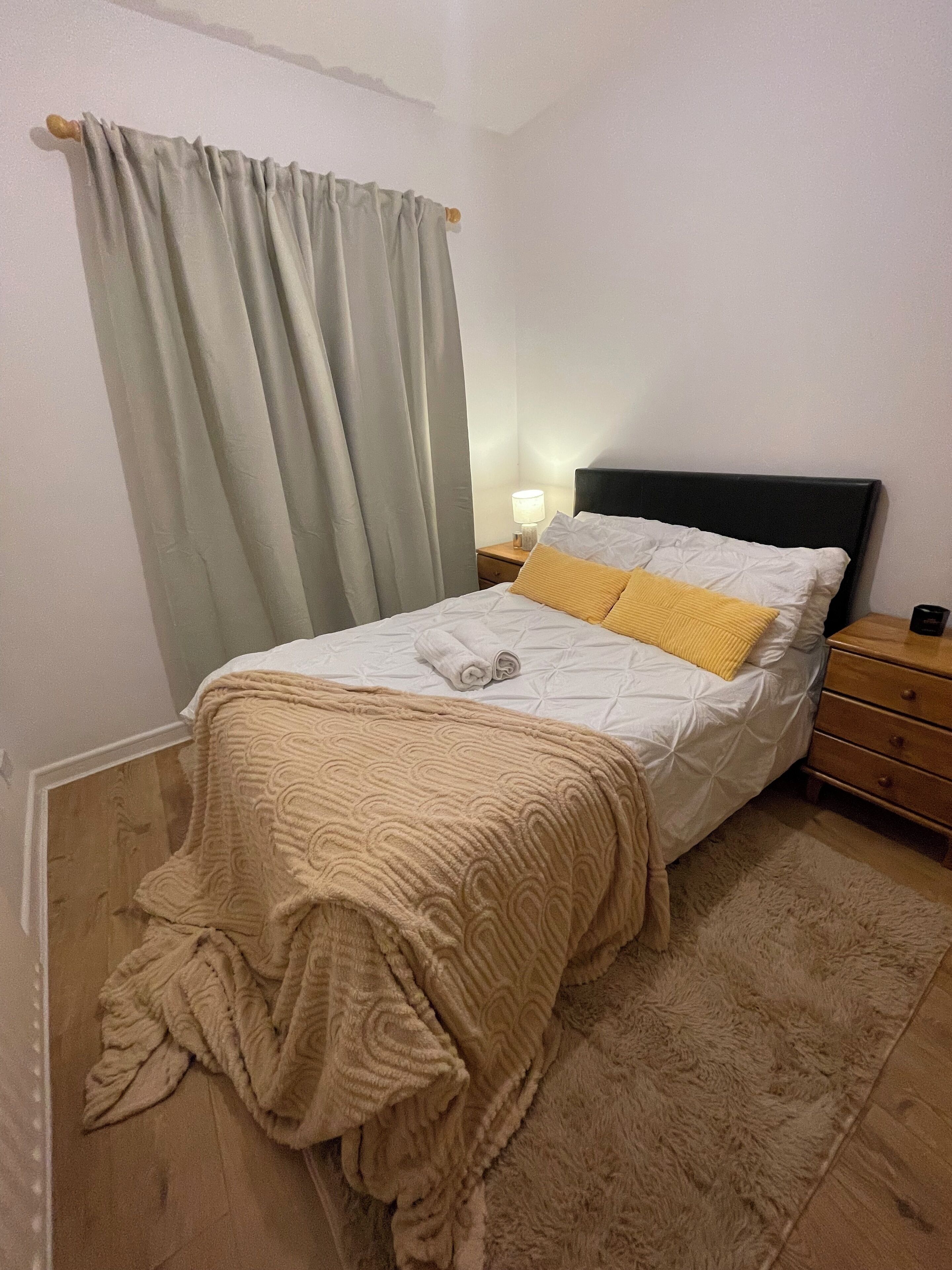 Una cama bien hecha con un edredón estampado, una lámpara de noche y una mesita de madera.