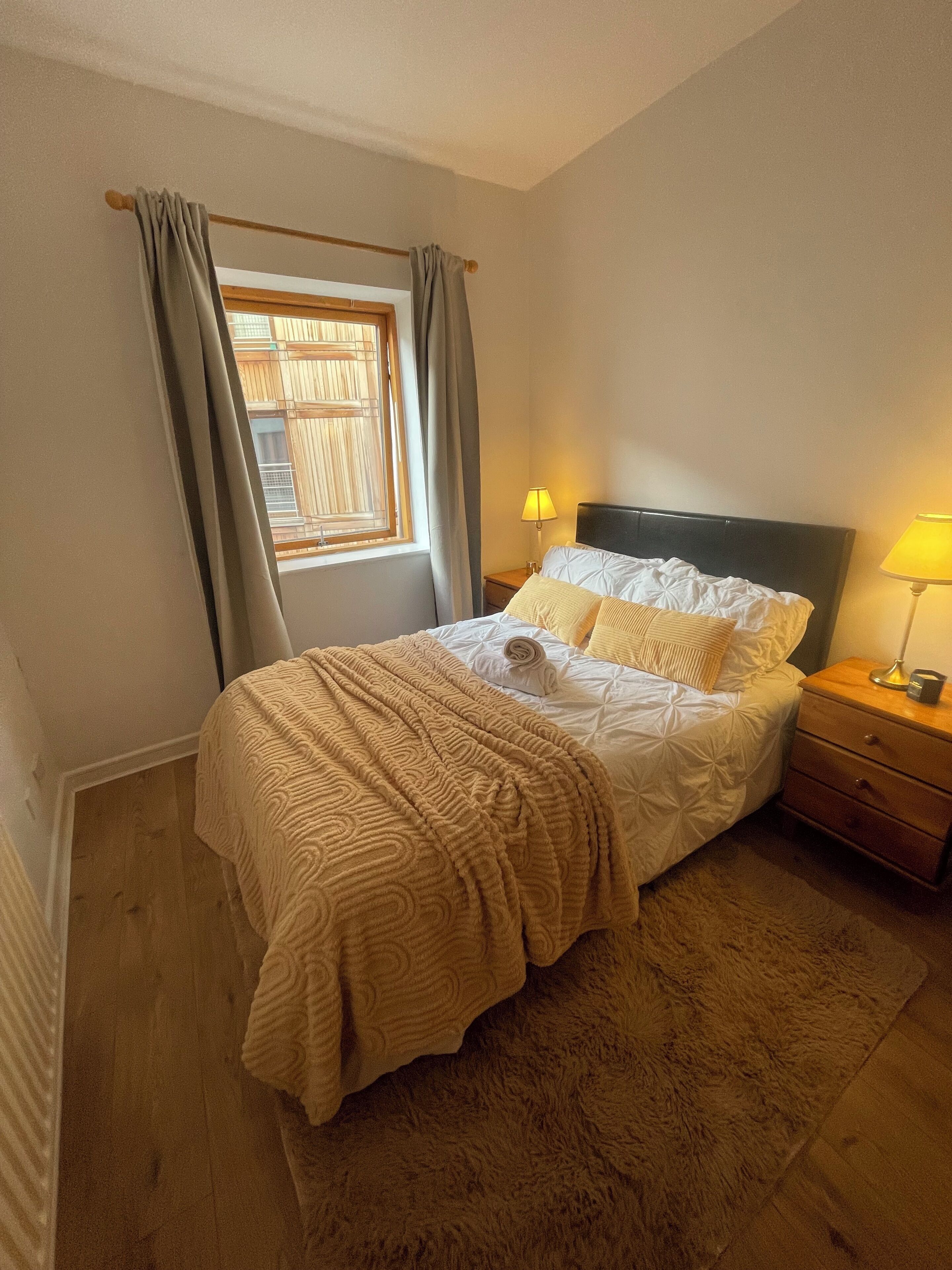 A bedroom with a bed, two bedside tables, a window with curtains, and a lamp on each table.