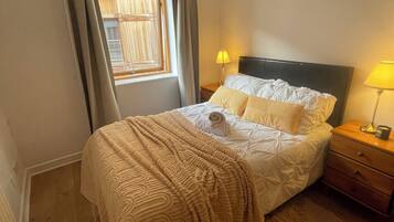 A bedroom with a bed, two bedside tables, a window with curtains, and a lamp on each table.