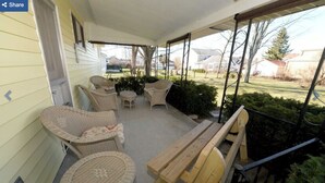 A covered porch with wicker furniture, a wooden bench, and a view of the yard.
