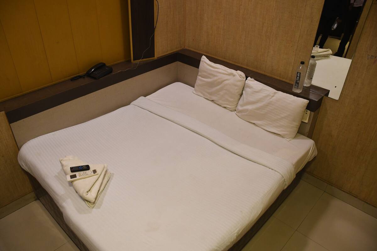 Un lit bien fait, avec des oreillers, une serviette pliée et une télécommande posée sur le lit.