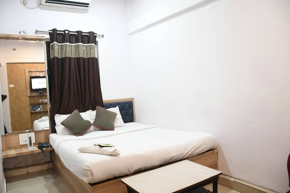 Une chambre d’hôtel avec un lit, une table de chevet, un miroir et un téléviseur fixé au mur.