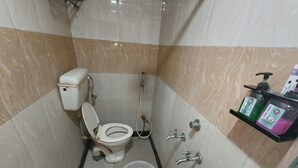Une salle de bain équipée de toilettes, d’un bidet et d’un lavabo. Un seau et un distributeur de savon sont fixés au mur.