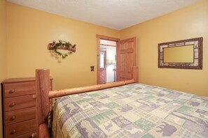 Un dormitorio con estructura de cama de madera, cómoda de madera, un espejo y una puerta que da a otra habitación.